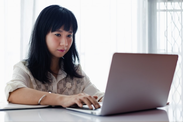 Femme asiatique utilisant un ordinateur portable et travaillant à la maison pour les affaires, l'auto-quarantaine, le maintien à la maison et la distance sociale dans le concept de situation d'épidémie de coronavirus ou de Covid-2019