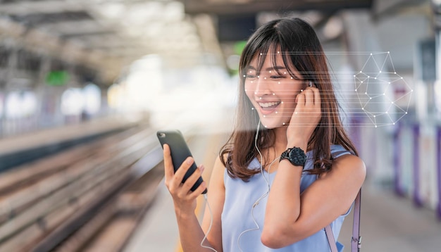 Femme asiatique utilisant la reconnaissance faciale via un téléphone mobile intelligent et écoutant de la musique à Railroad