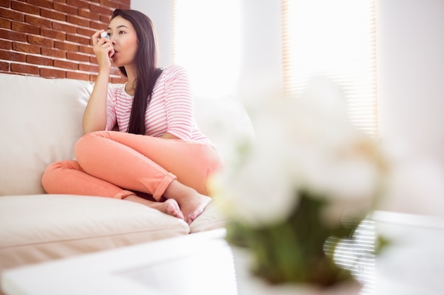 Femme asiatique en utilisant son inhalateur sur le canapé