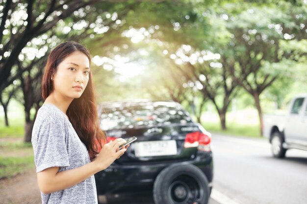 Femme asiatique en utilisant le téléphone portable tout en regardant et Stress assis après la panne de voiture