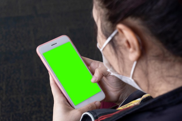 Une femme asiatique utilise un écran vert de smartphone avec un visage de masque chirurgical