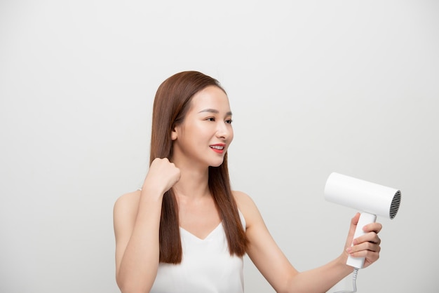 Une femme asiatique utilise un sèche-cheveux sur fond blanc