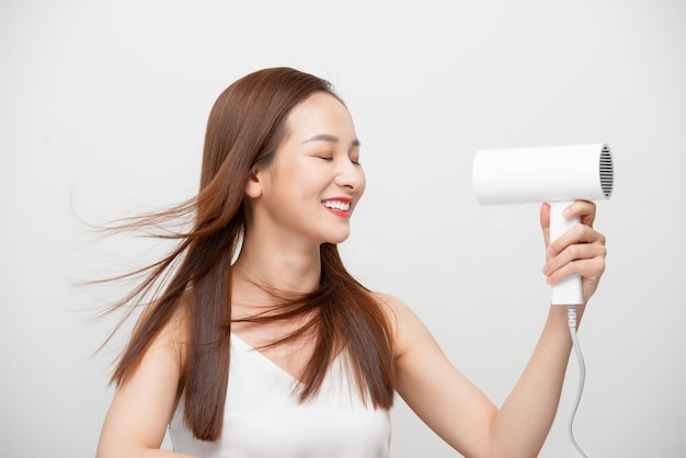 Une femme asiatique utilise un sèche-cheveux sur fond blanc