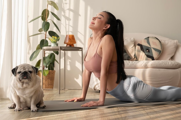 Une femme asiatique en vêtements de sport faisant de l'exercice et du yoga avec un mignon chien dans le salon à la maison