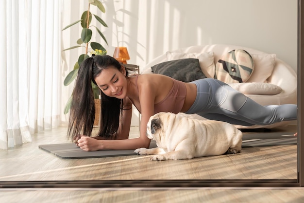 Une femme asiatique en vêtements de sport faisant de l'exercice et du yoga avec un mignon chien dans le salon à la maison