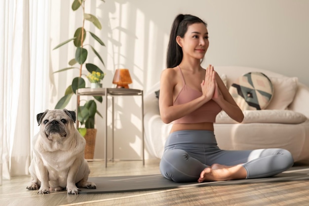 Une femme asiatique en vêtements de sport faisant de l'exercice et du yoga avec un mignon chien dans le salon à la maison