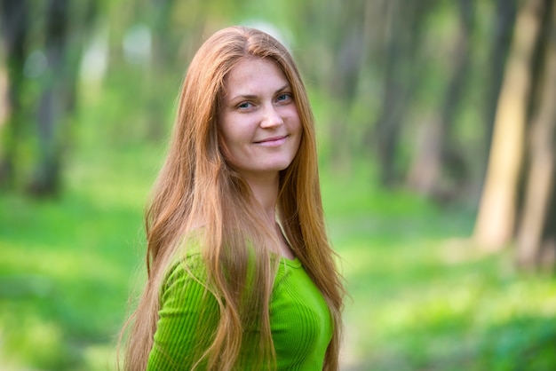 Femme assez heureuse avec de longs cheveux rouges dans le parc de printemps vert