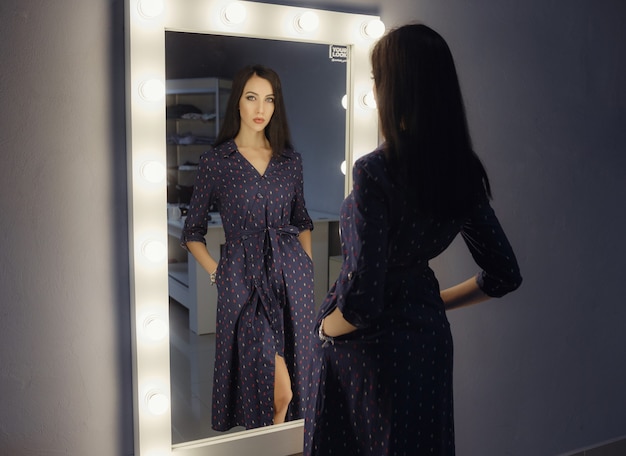 Femme assez heureuse regardant sur elle-même dans un grand miroir. La femme choisit une tenue pour les vacances