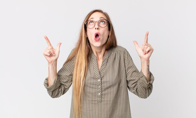 femme assez mince à l'air choqué, étonné et bouche ouverte, pointant vers le haut avec les deux mains pour copier l'espace