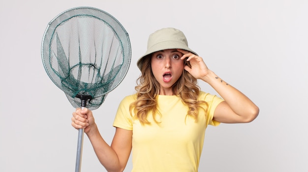 Femme assez mince ayant l'air heureuse, étonnée et surprise portant un chapeau et tenant un filet de pêche