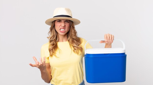 Femme assez mince qui a l'air en colère, agacée et frustrée et tient un réfrigérateur de pique-nique d'été