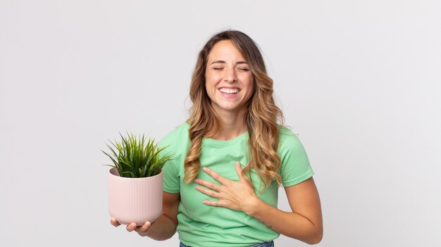 Femme assez mince riant aux éclats d'une blague hilarante et tenant une plante décorative