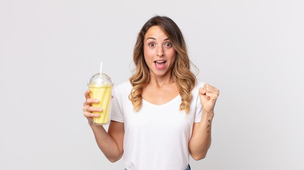 Femme assez mince se sentant choquée, riant et célébrant le succès et tenant un milk-shake à la vanille