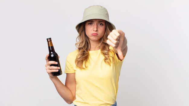 Femme assez mince se sentant croisée, montrant les pouces vers le bas et tenant une bière. concept d'été