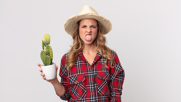 Femme assez mince se sentant dégoûtée et irritée et tirant la langue tenant un cactus. concept d'agriculteur