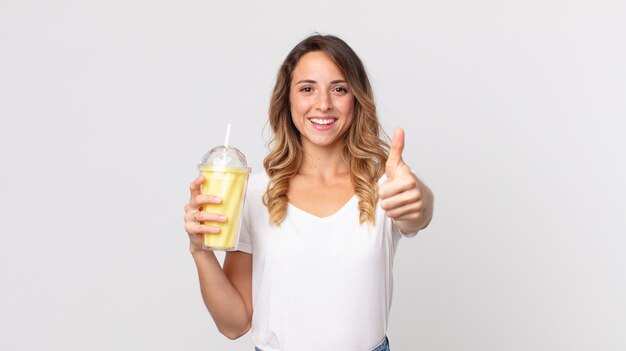 femme assez mince se sentant fière, souriant positivement avec les pouces vers le haut et tenant un milk-shake à la vanille