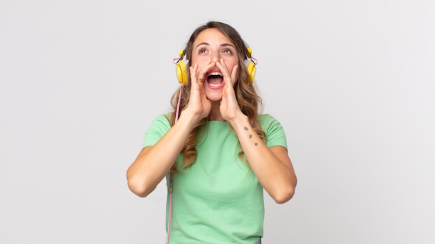 Femme assez mince se sentant heureuse, donnant un grand cri avec les mains à côté de la bouche écoutant de la musique avec des écouteurs