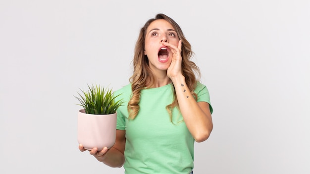 Femme assez mince se sentant heureuse, donnant un grand cri avec les mains à côté de la bouche et tenant une plante décorative