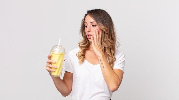 Femme assez mince se sentant heureuse, excitée et surprise et tenant un milk-shake à la vanille