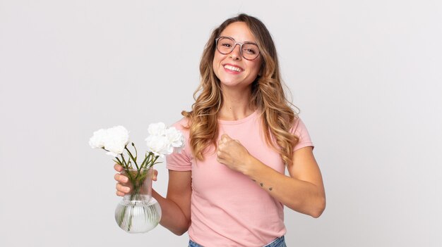 Femme assez mince se sentant heureuse et face à un défi ou célébrant et tenant des fleurs décoratives