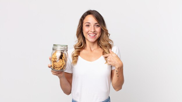 Femme assez mince se sentant heureuse et se montrant elle-même avec une bouteille en verre de biscuits excitée et tenant