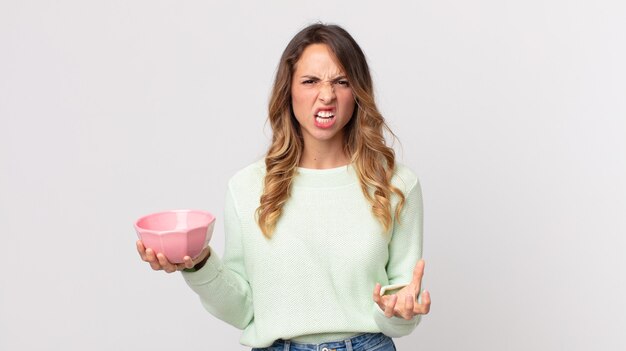 Femme assez mince semblant en colère, agacée et frustrée et tenant un bol de pot vide