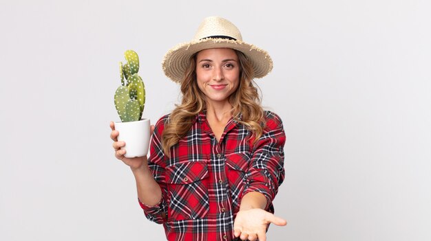 Femme assez mince souriant joyeusement avec amicale et offrant et montrant un concept tenant un cactus. concept d'agriculteur