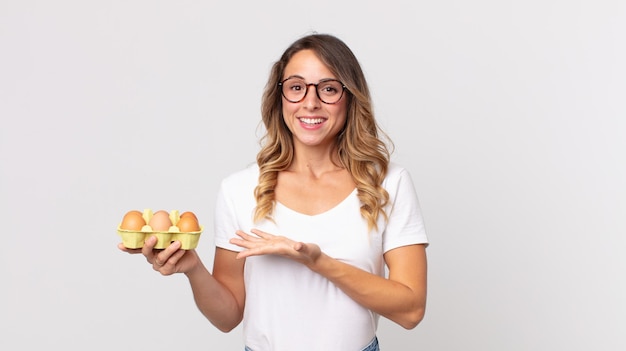 Femme assez mince souriant joyeusement, se sentant heureuse et montrant un concept et tenant une boîte à œufs