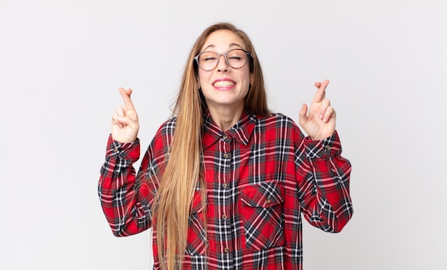 Femme assez mince souriante et croisant anxieusement les deux doigts, se sentant inquiète et souhaitant ou espérant bonne chance