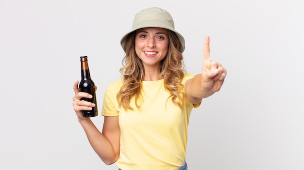 Femme assez mince souriante et semblant amicale, montrant le numéro un et tenant une bière. concept d'été