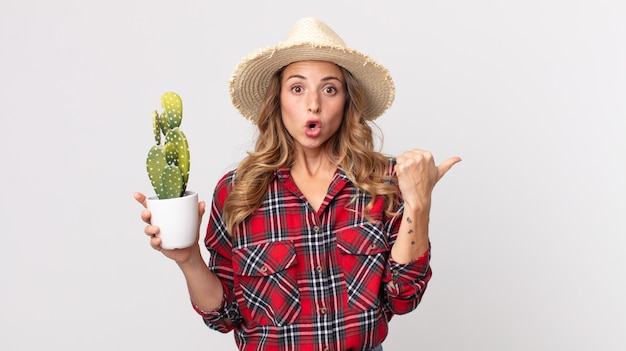 Femme assez mince à la stupéfaction d'incrédulité tenant un cactus. concept d'agriculteur