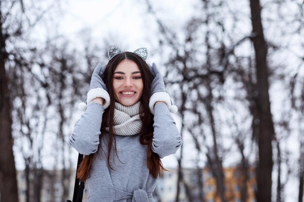 Femme assez à la mode vêtue de gants habillés gris et d'un bandeau de chat à l'extérieur dans le parc d'hiver