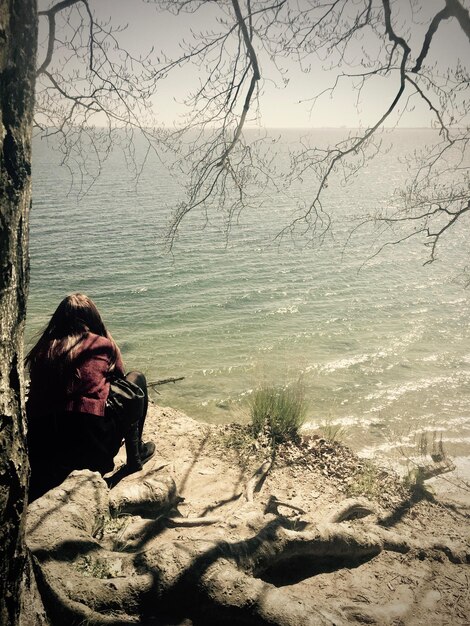 Photo une femme assise sur un arbre nu contre le ciel