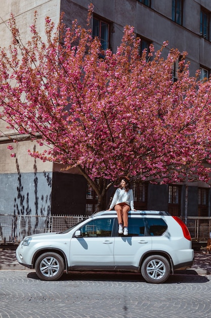 Femme assise sur l'arbre de sakura en fleurs de voiture sur fond le printemps arrive
