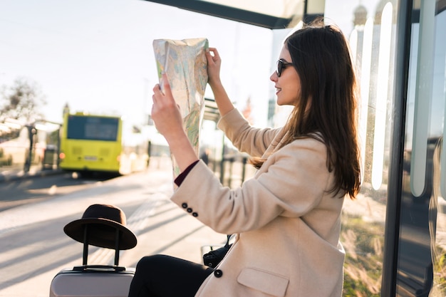 Femme assise à l'arrêt de bus nad tenant le plan de la ville.