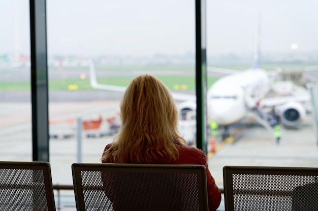 Femme assise et attendant son vol dans le hall de départ de l'aéroport de Milan-Bergame en Italie. Avion sur le fond