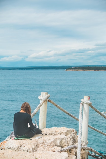 Femme assise au bord, dessinant une photo de paysage marin