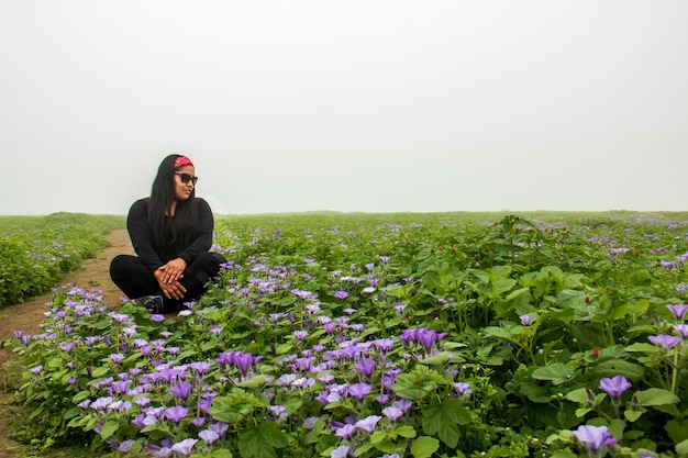 Femme assise au milieu du chemin des plantes vertes fleurs lilas et ciel nuageux