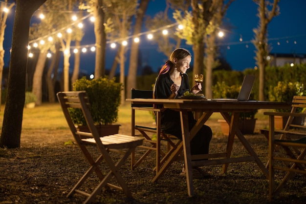 Femme assise au restaurant en plein air avec ordinateur portable le soir à l'extérieur. Se reposer et travailler à l'hôtel sur la nature. Concept de week-end, repos et vacances. Idée de loisir