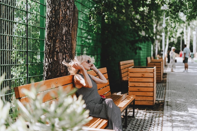 Femme assise sur un banc en bois dans un parc d'été avec des arbres verts et un fond ensoleillé avec de l'herbe et