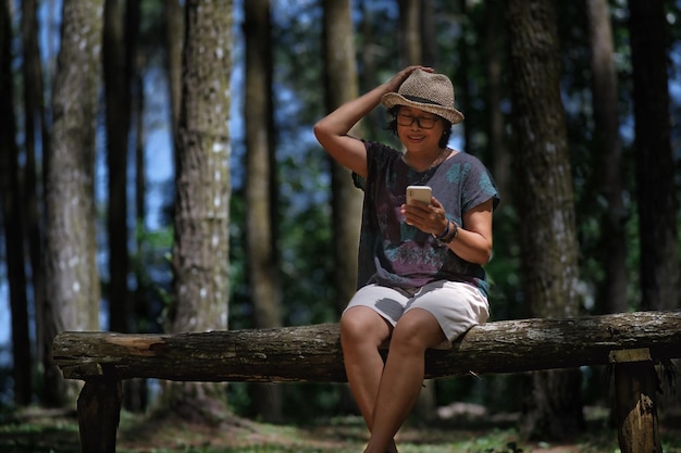 Une femme assise sur un banc de bois dans le parc en lisant des messages sur son smartphone