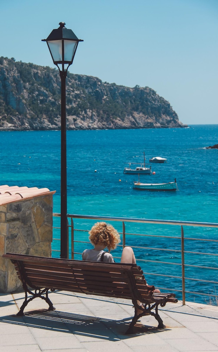 Photo une femme assise sur un banc face à la mer.