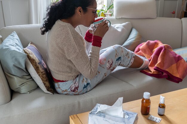 Photo une femme assise sur un canapé blanc dans le salon buvant du thé et se sentant malade.