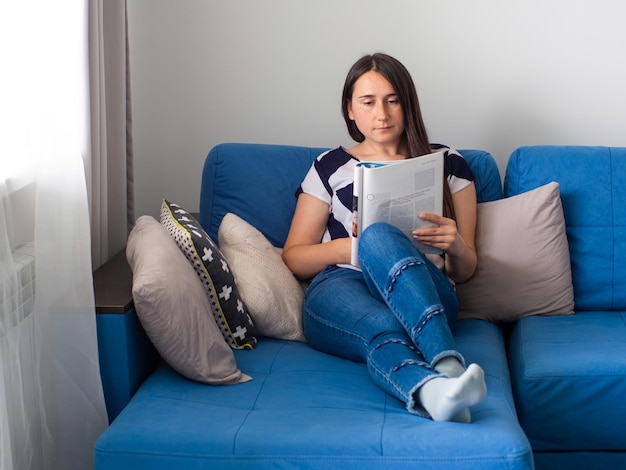 Femme assise sur un canapé bleu dans le salon et lisant les nouvelles