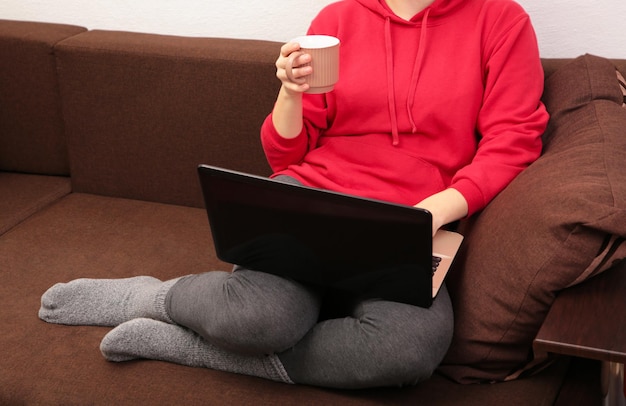 Femme assise sur un canapé confortable écrivant des e-mails sur un ordinateur portable et buvant du café, fille indépendante travaillant à l'ordinateur depuis la maison, étudiante concentrée étudiant un lit.