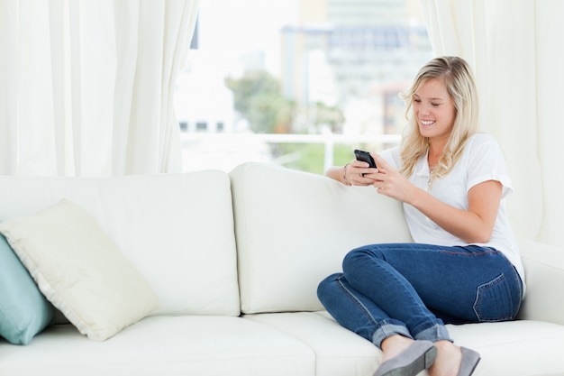 Une femme assise sur le canapé sur le côté pendant qu&#39;elle utilise son téléphone