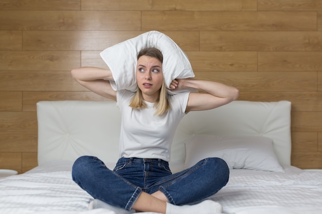 femme assise sur le canapé couvre les oreilles avec les mains agacées par le bruit