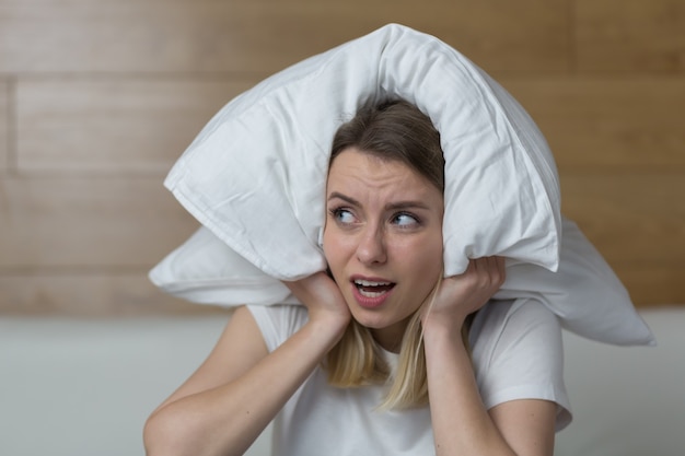 femme assise sur le canapé couvre les oreilles avec les mains agacées par le bruit