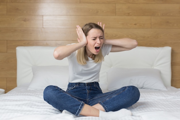 femme assise sur le canapé couvre les oreilles avec les mains agacées par le bruit