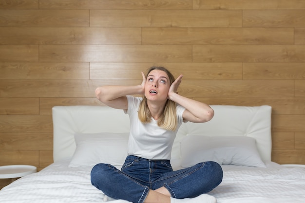 femme assise sur le canapé couvre les oreilles avec les mains agacées par le bruit